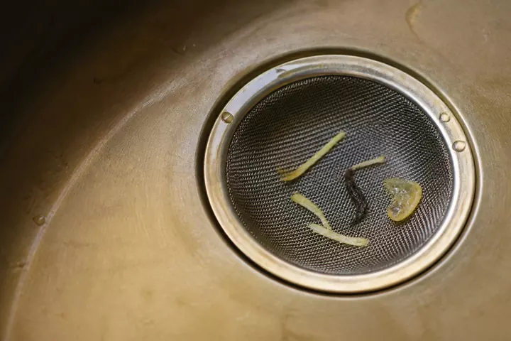 Ginger threads, tea leaf and lemon pulp in a brass-toned sink strainer