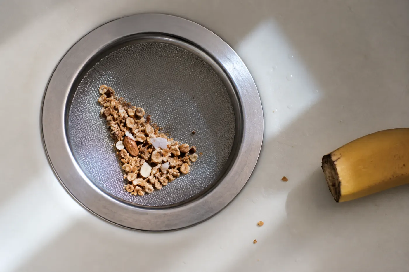 Granola, coconut flakes and an almond sliver in a fine mesh strainer beside a banana end