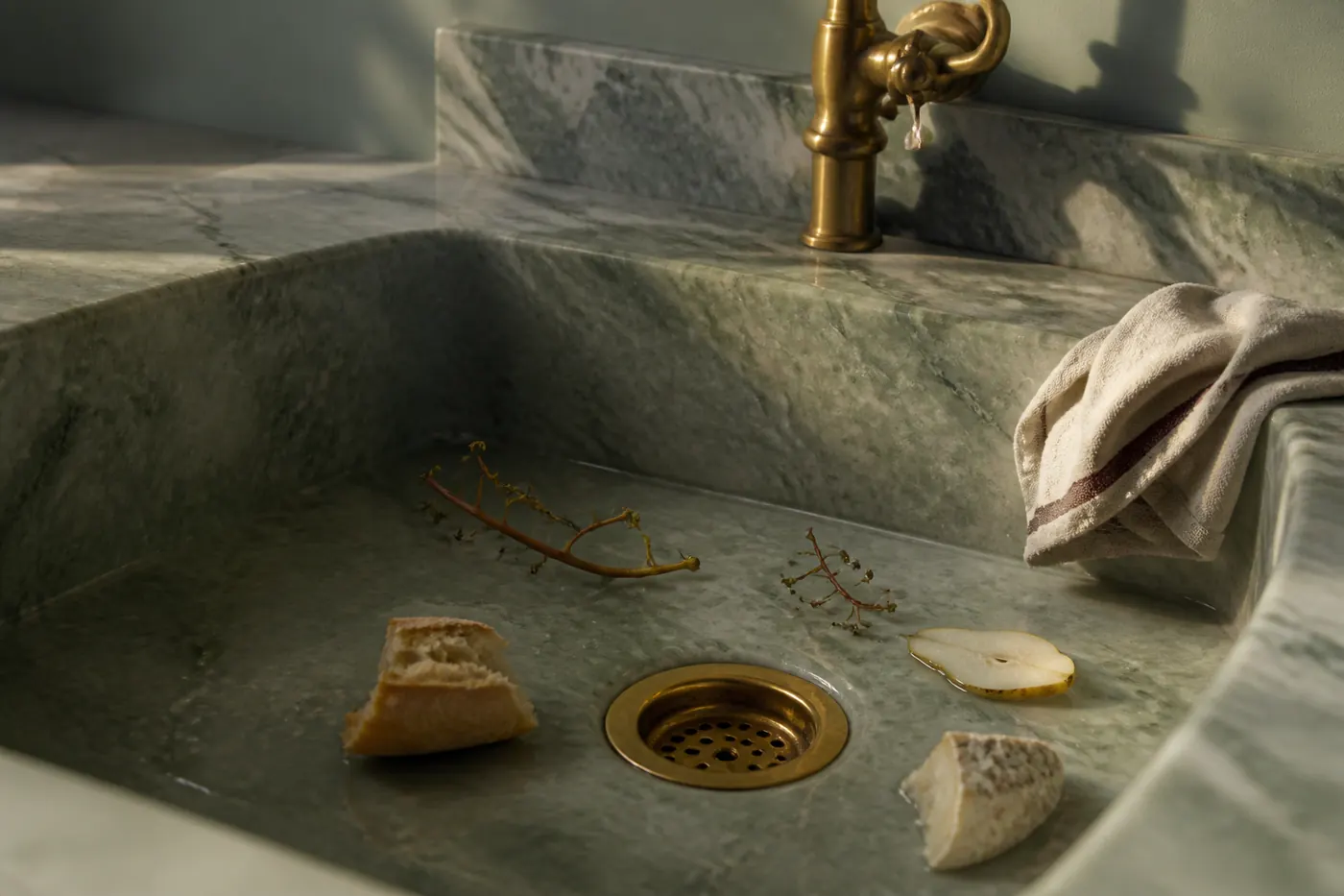 Green marble sink containing a pear slice, bread, grape stems and cheese rind