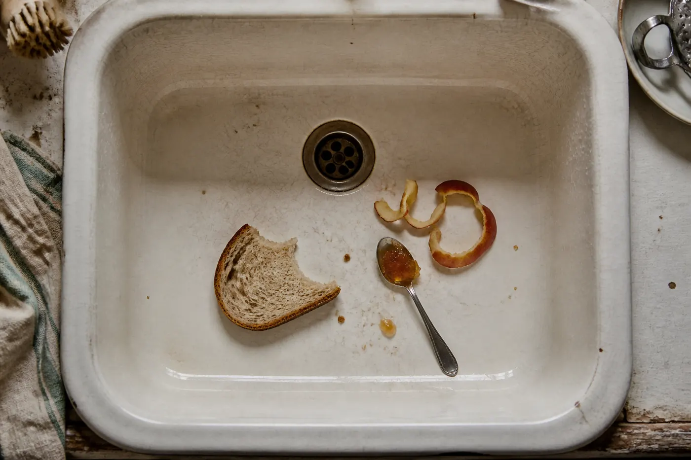 White farmhouse sink holding bread, apple peel and a spoonful of marmalade