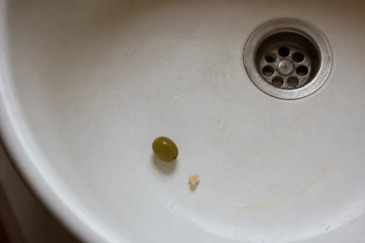 Single green olive, bread crumb and oil trace in white porcelain