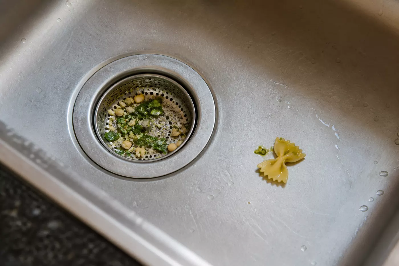 Basil, pine nut and Parmesan caught in a steel strainer beside one pesto-marked pasta bow
