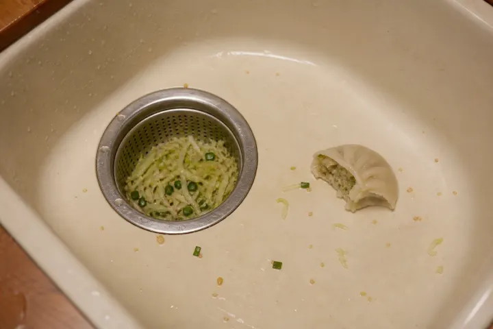 Pasta and ricotta caught in a strainer beside half a raviolo